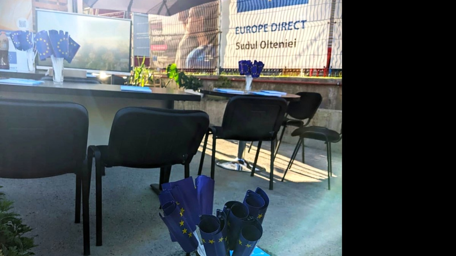 Punct de informare în aer liber, cu mese, scaune și stegulețe ale Uniunii Europene pregătite pentru participanți.