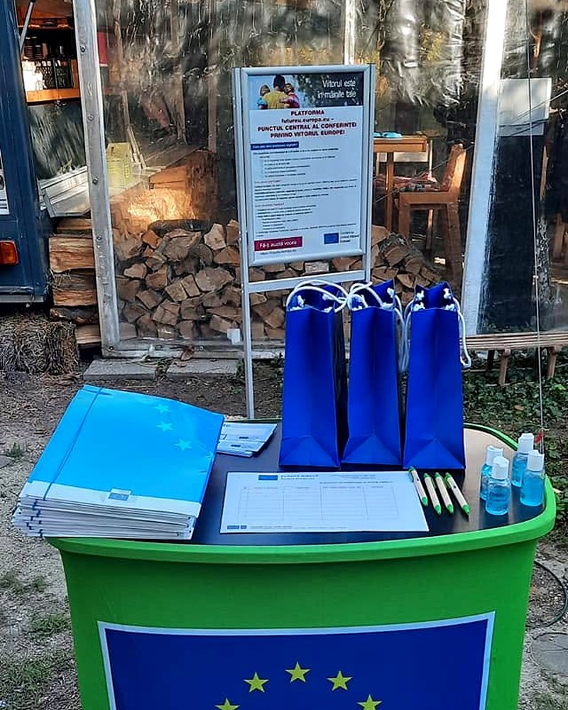 Stand de informare cu emblema Uniunii Europene, pe care sunt așezate broșuri și postere rulate.