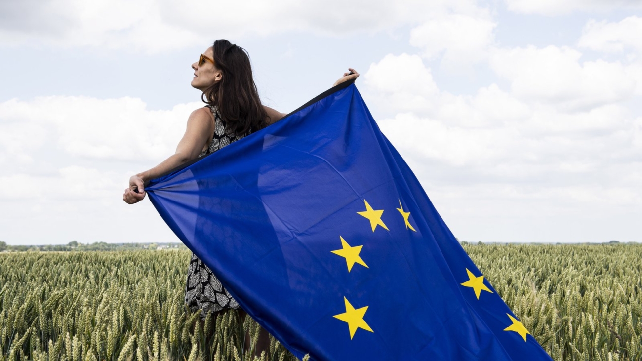 Femeie ținând steagul Uniunii Europene într-un lan de grâu